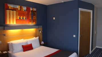 A hotel room with a bed, a nightstand, a wall-mounted lamp, a painting, and a door.