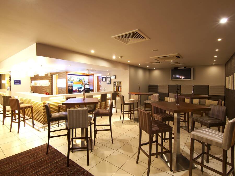 A hotel lobby with a bar area, seating arrangements, and a television mounted on the wall.