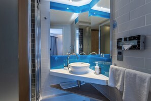 A modern bathroom with a large mirror, a white sink, and a blue accent wall.