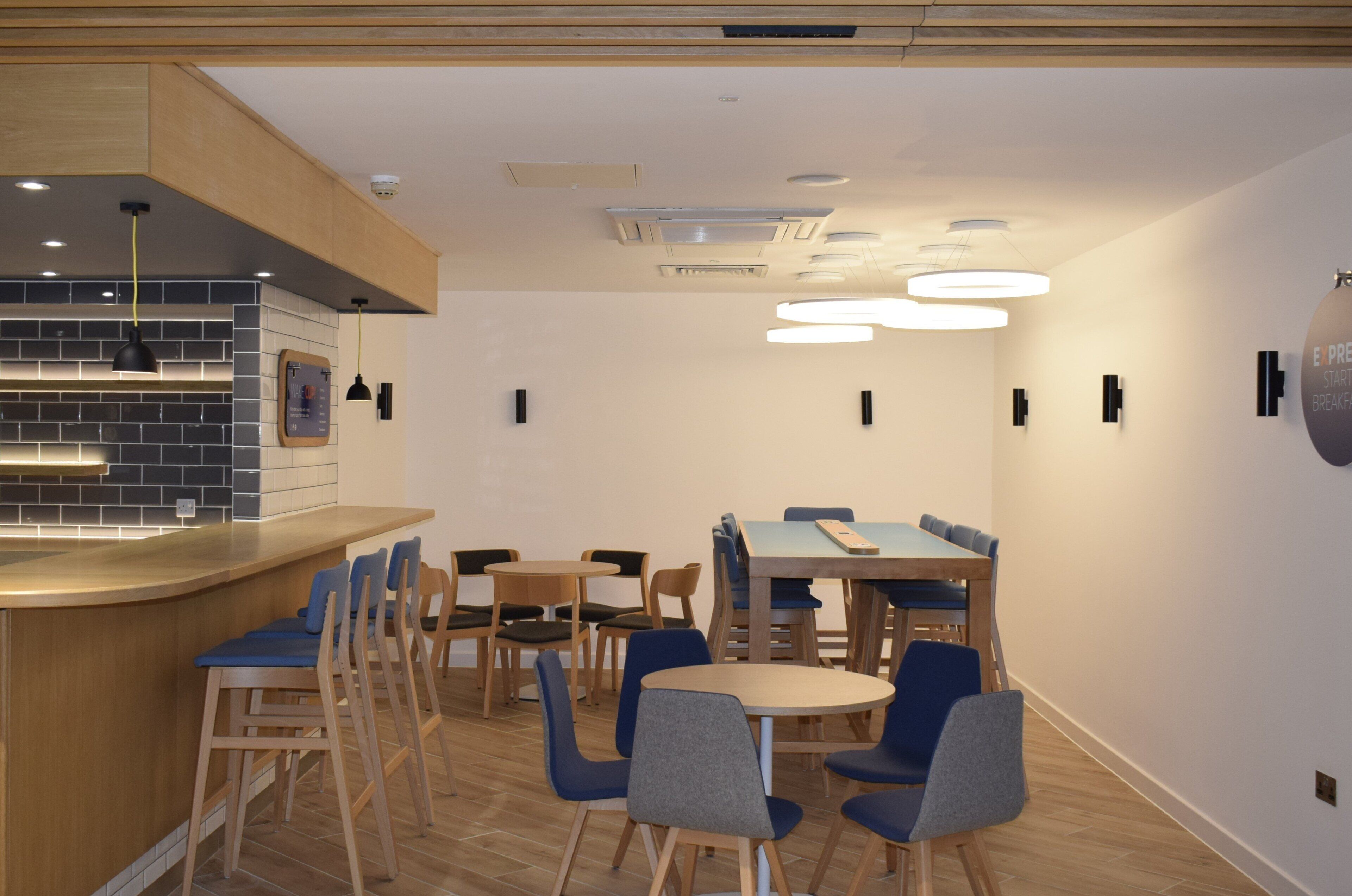 A modern dining area with a bar, wooden chairs, and a mix of round and rectangular tables.