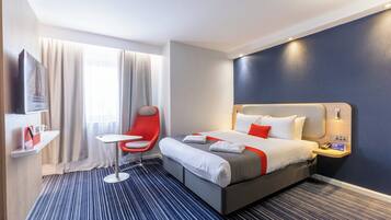 Una habitación de hotel con una cama, una silla roja, una mesita, un televisor y una ventana con cortinas.