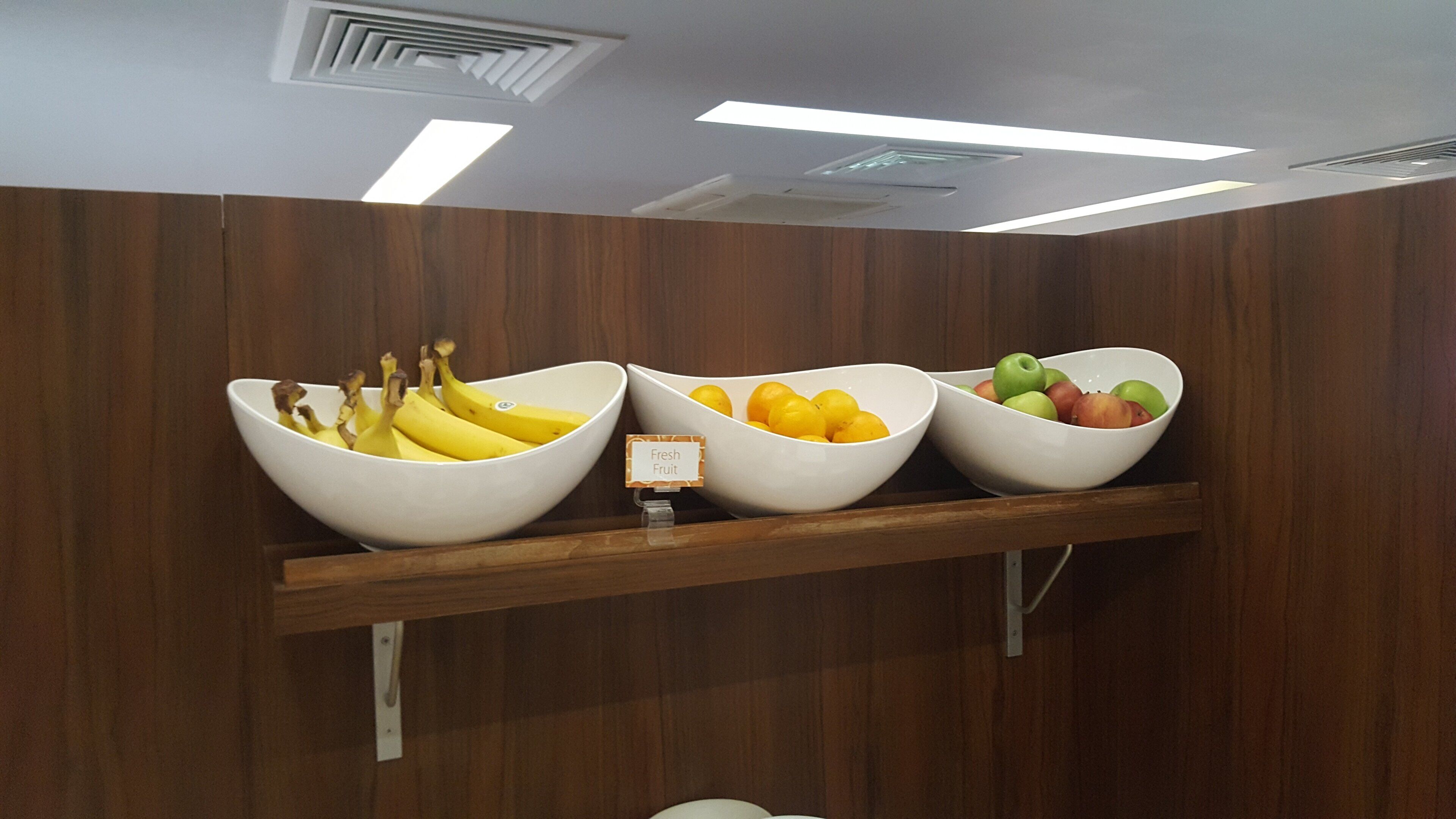 A wooden-framed shelf with three white bowls containing bananas, lemons, and apples.