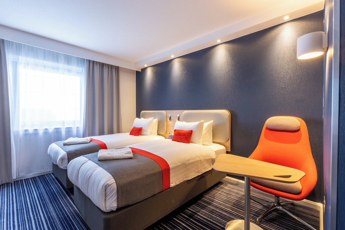 A hotel room with two beds, a desk, and a chair.
