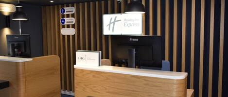 Un mostrador de recepción con un cartel de Holiday Inn Express, una pantalla digital y una cámara de seguridad.