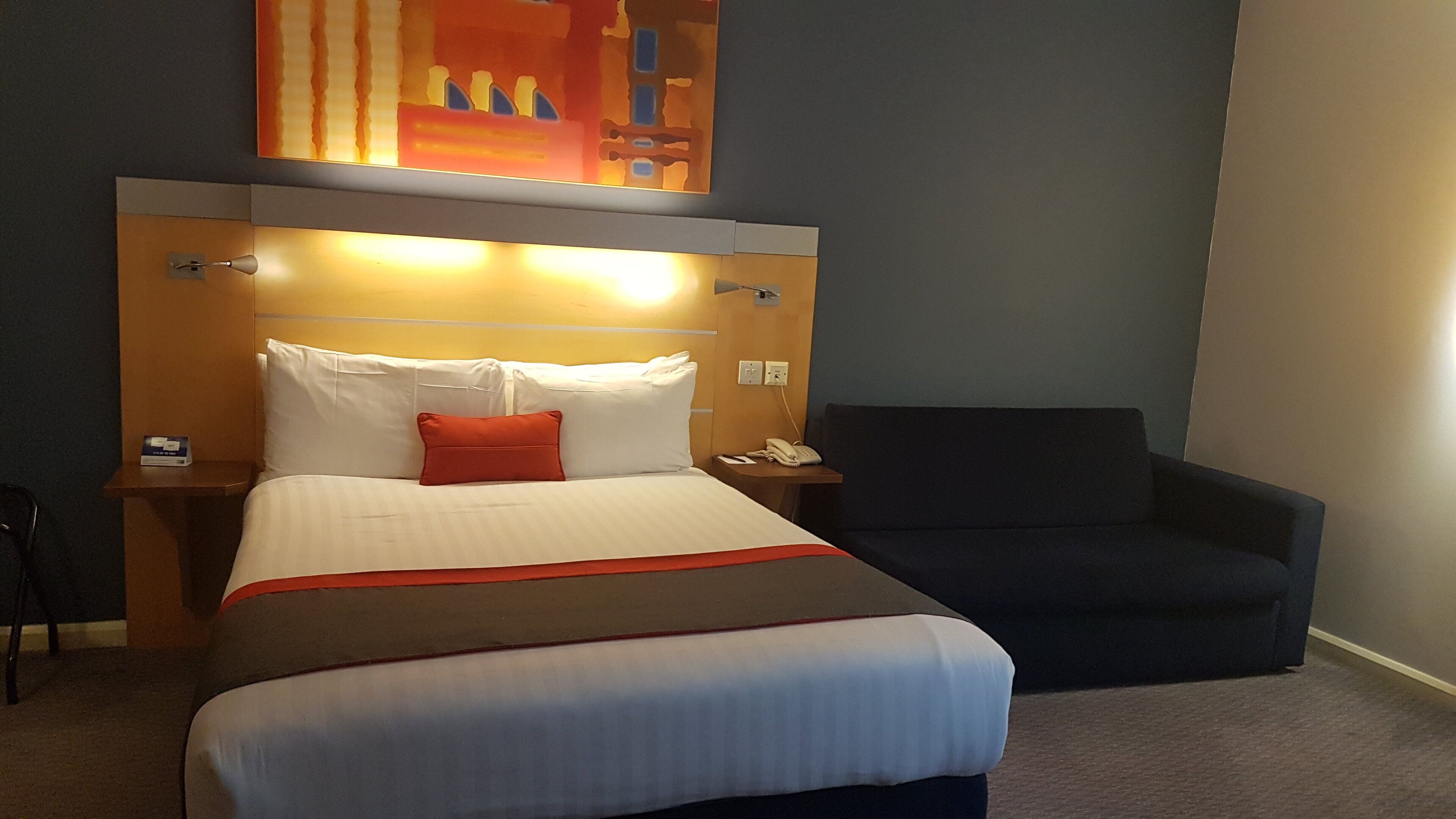 A hotel room with a bed, a nightstand, a chair, and a painting on the wall.