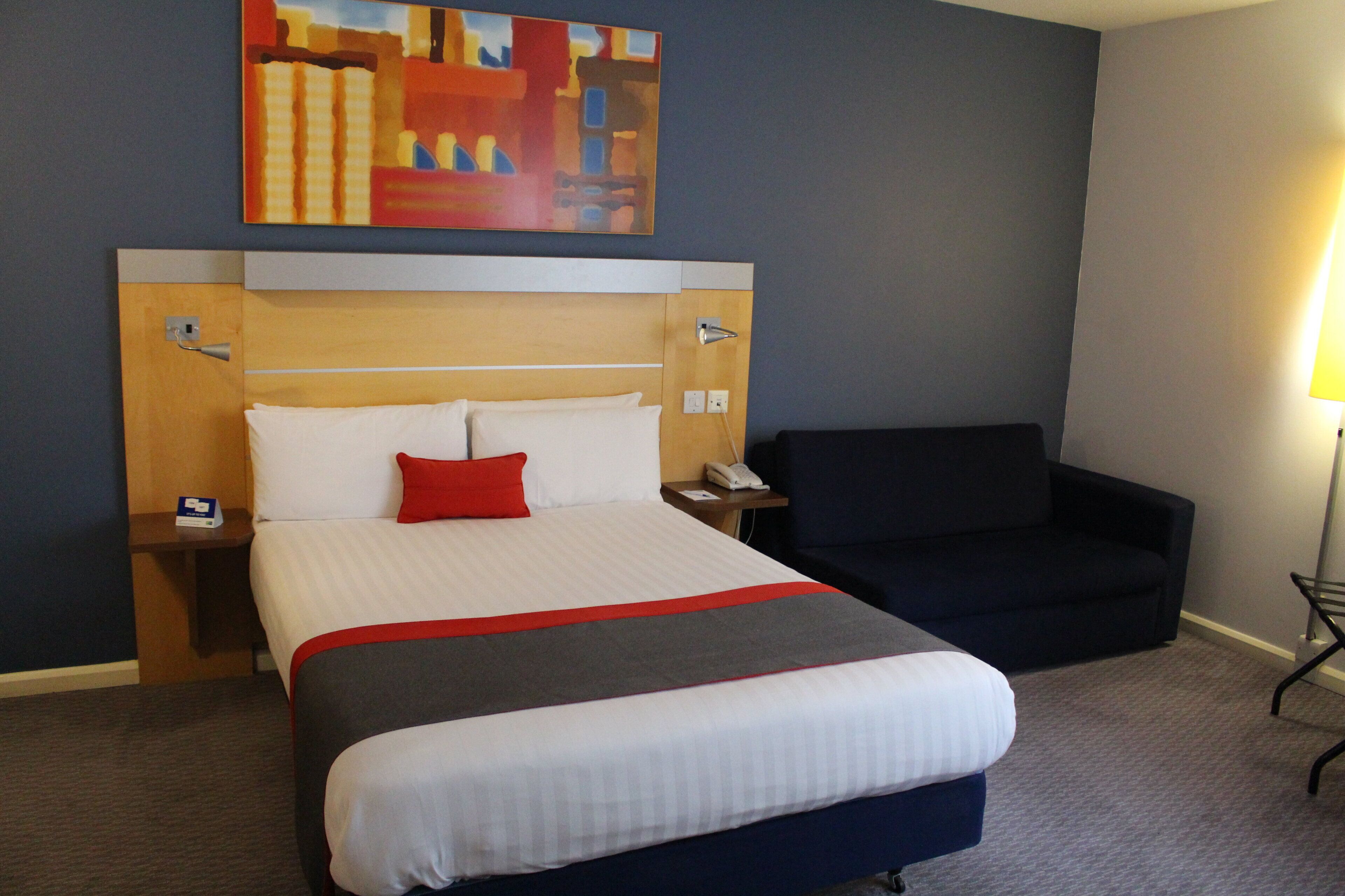 Une chambre d’hôtel avec un lit, une chaise, un tableau au mur et une lampe.