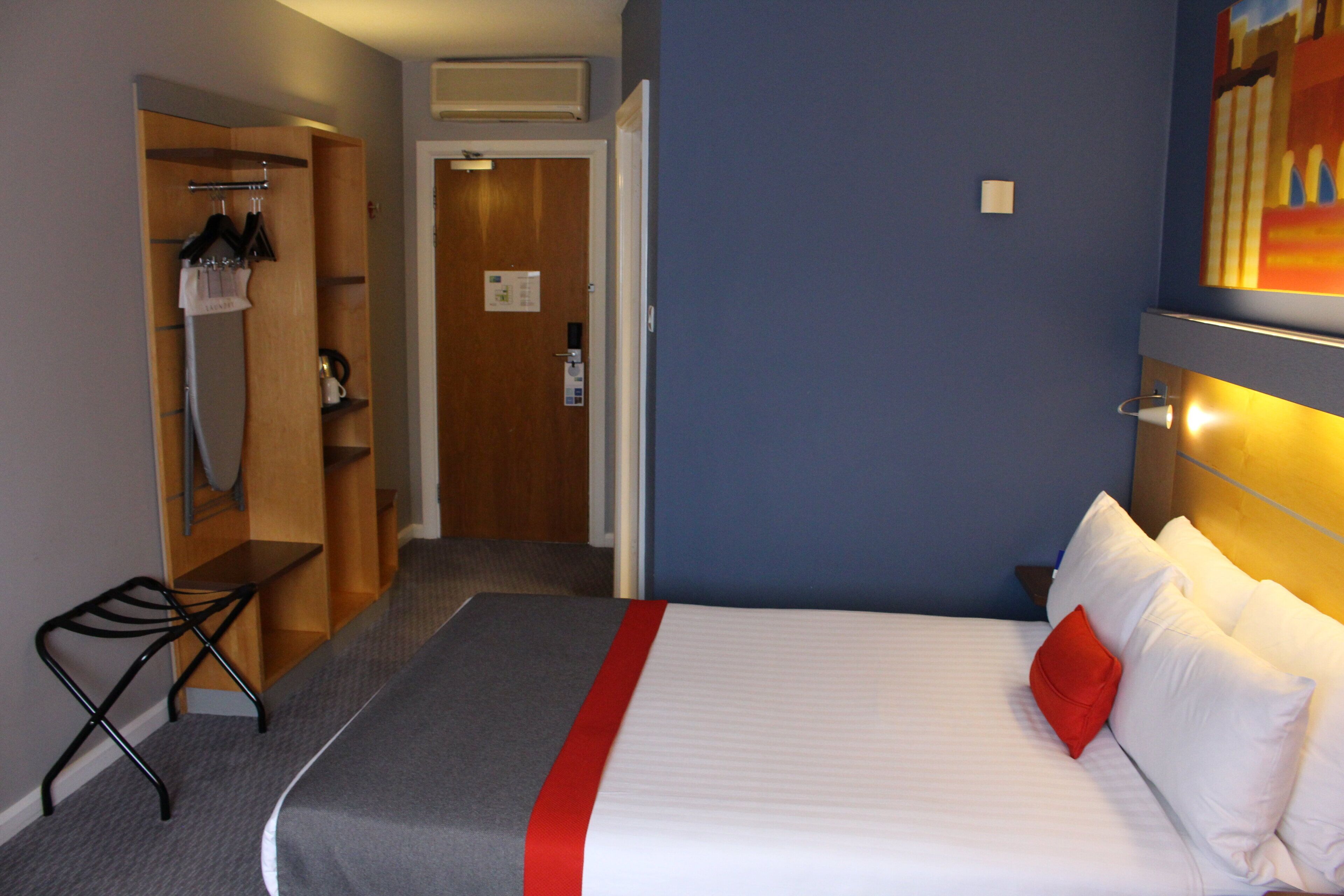 A hotel room with a bed, a desk, a chair, a wardrobe, and a shower area.