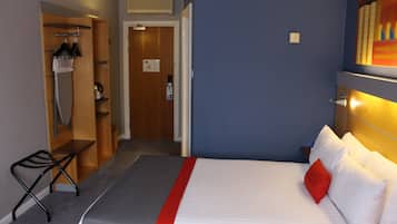 A hotel room with a bed, a desk, a chair, a wardrobe, and a shower area.