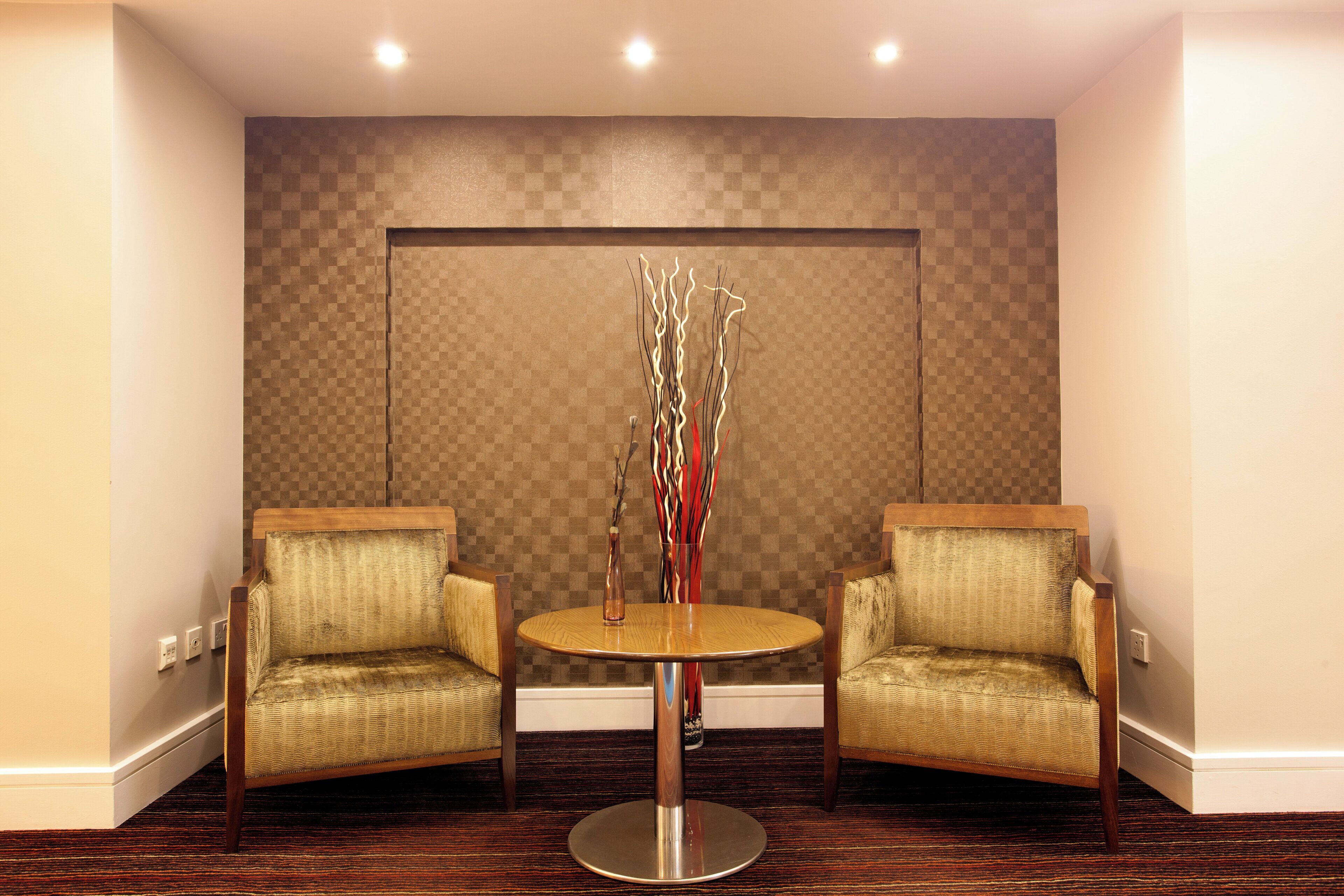 A hotel room with two armchairs, a round table, and a decorative vase with branches.
