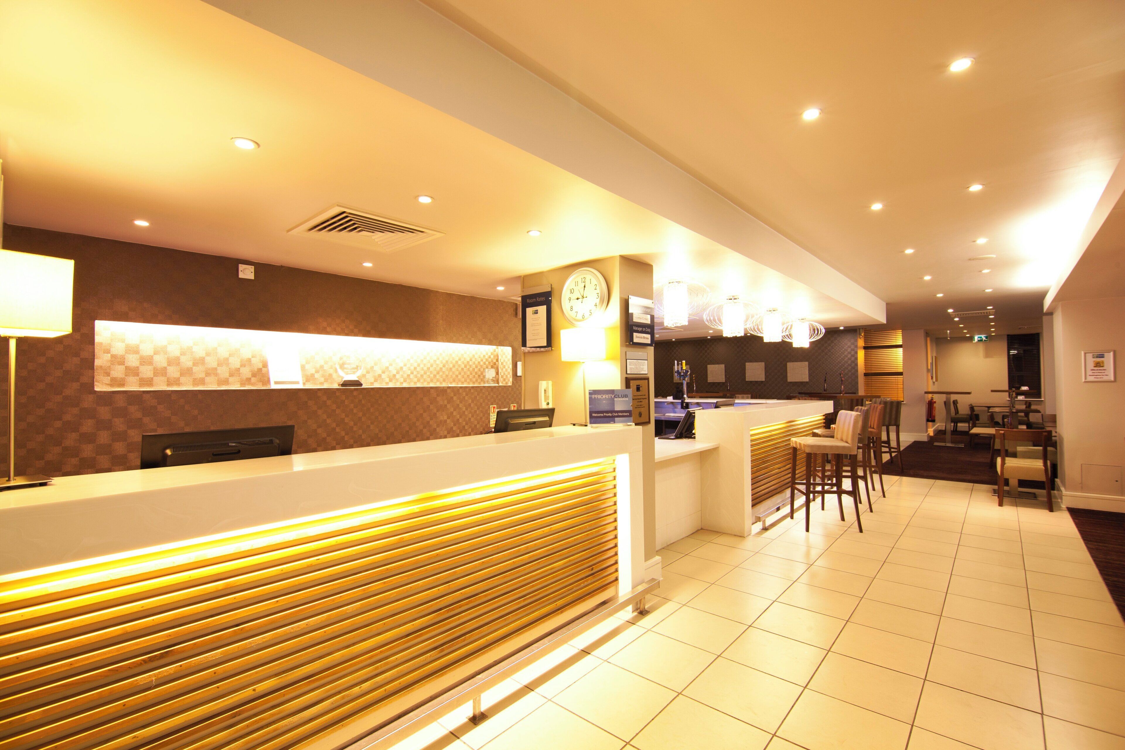 A hotel reception area with a check-in counter, a clock, and a bar area with stools.
