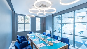 A conference room with a long table, blue chairs, and modern lighting fixtures.