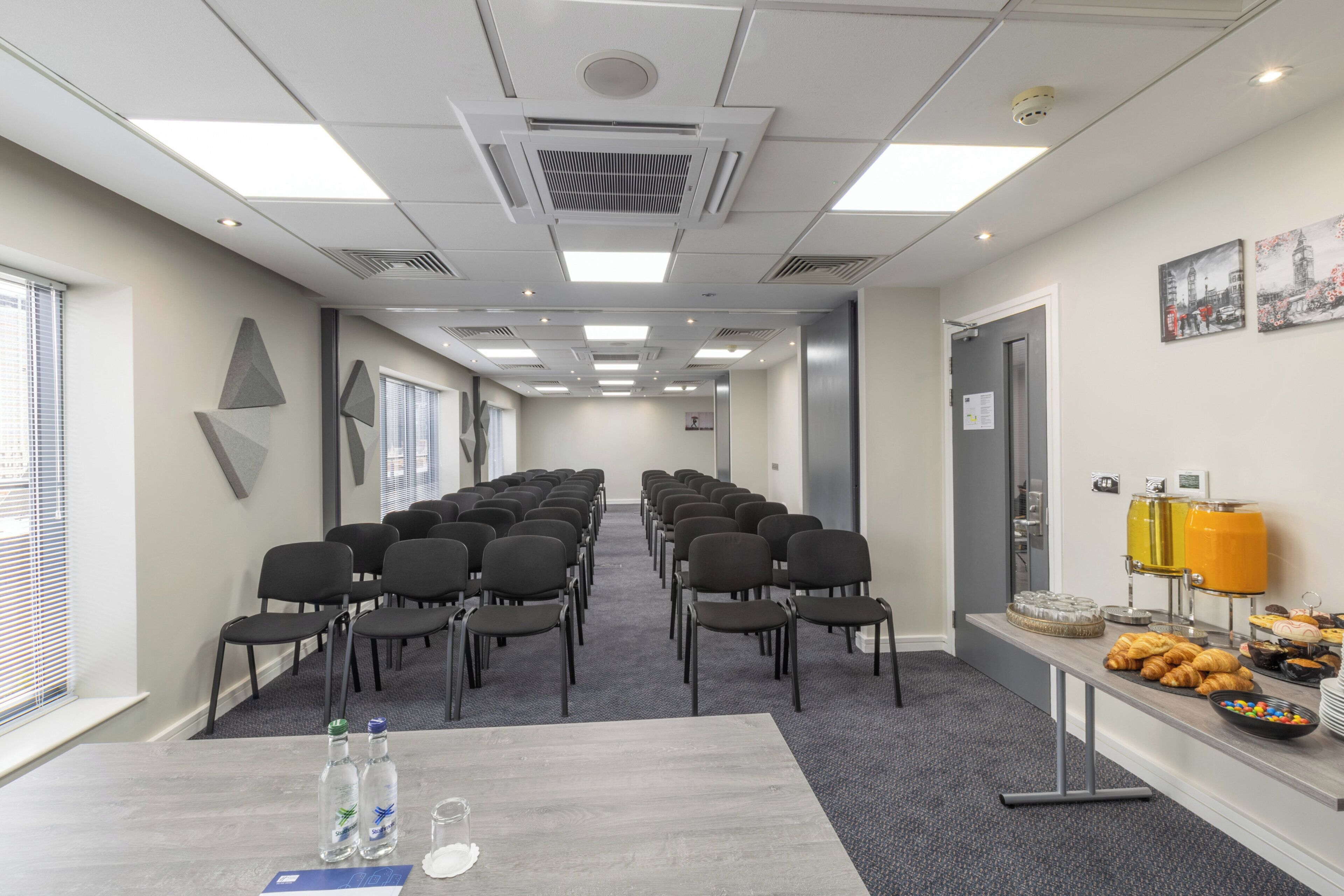 A conference room with rows of chairs, a buffet table with food and drinks, and a window with blinds.