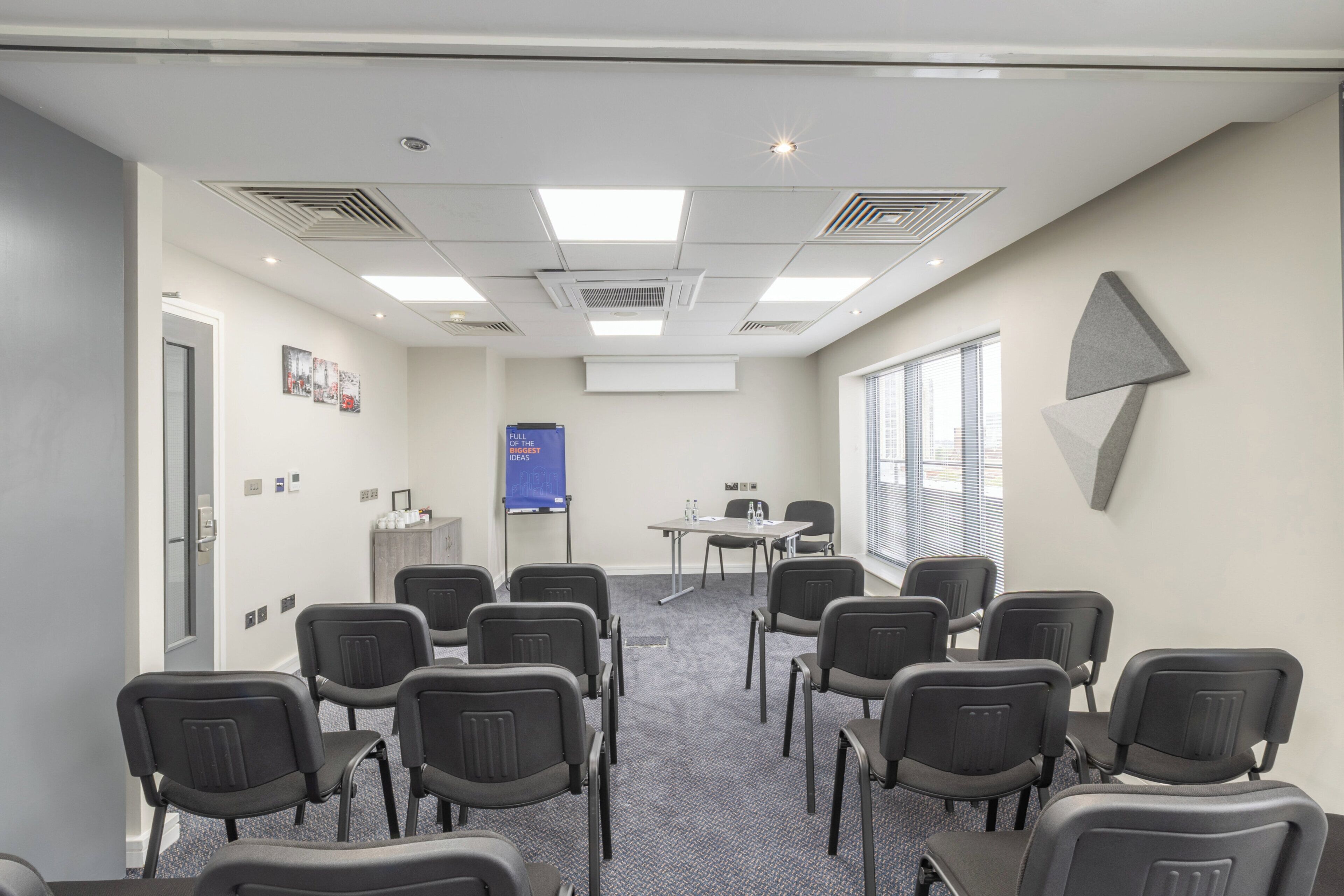 A conference room with rows of chairs, a whiteboard, and a projector screen.