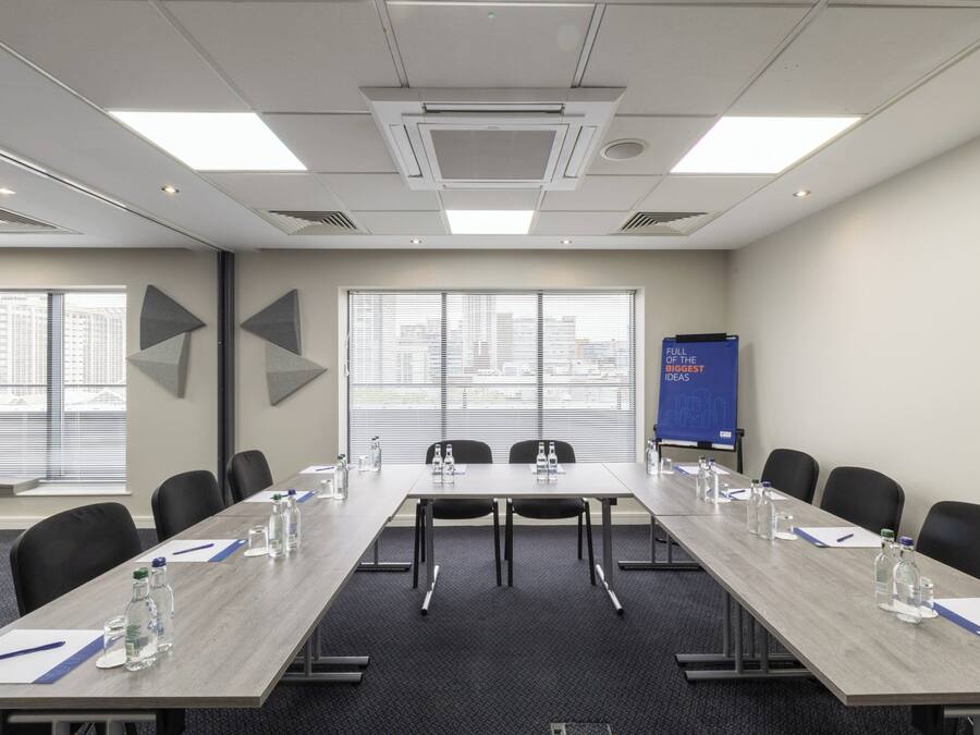Une salle de conférence avec une longue table, des chaises, des bouteilles d’eau et un écran de présentation.