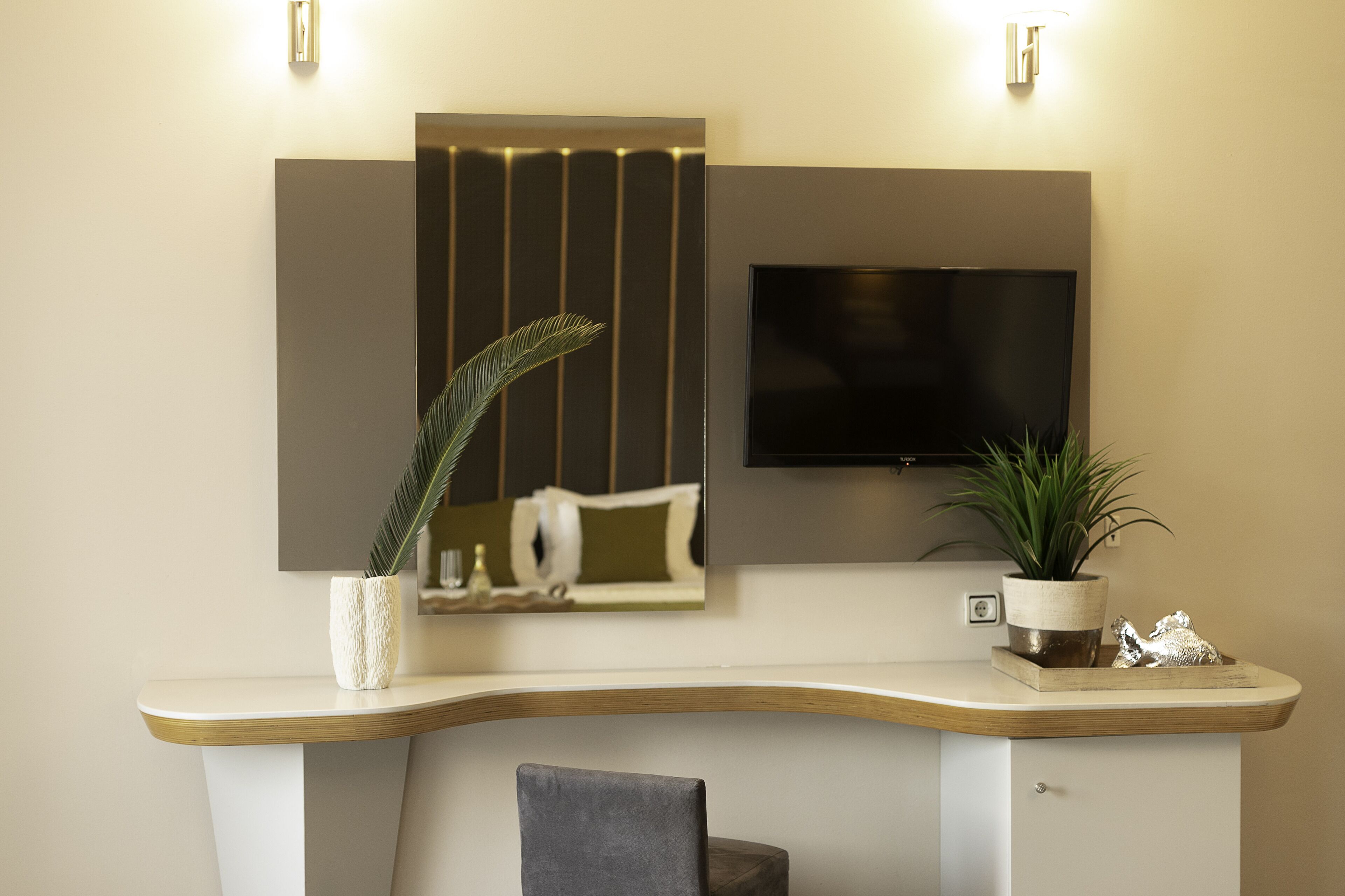 A modern living room with a curved white console table, a flat-screen TV mounted on the wall, and a potted plant on the table.
