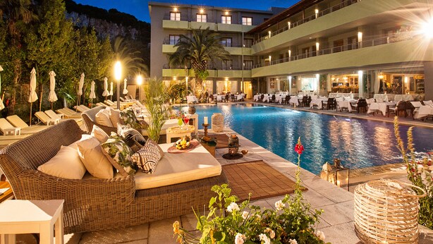 Un espace piscine d’hôtel comprenant des chaises longues, un canapé en osier et un coin repas.