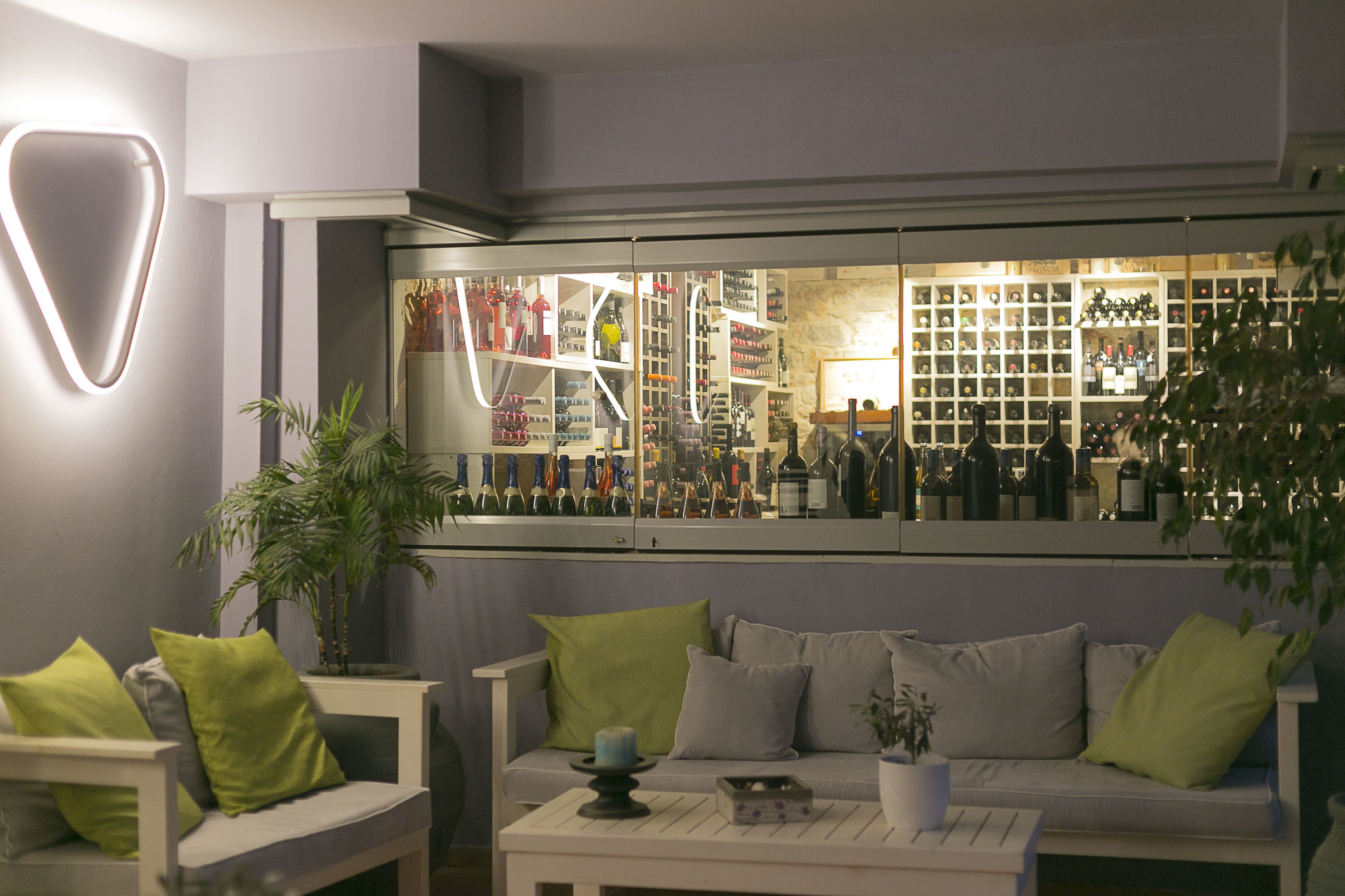 A modern interior with a seating area, a glass display case filled with bottles, and a potted plant.