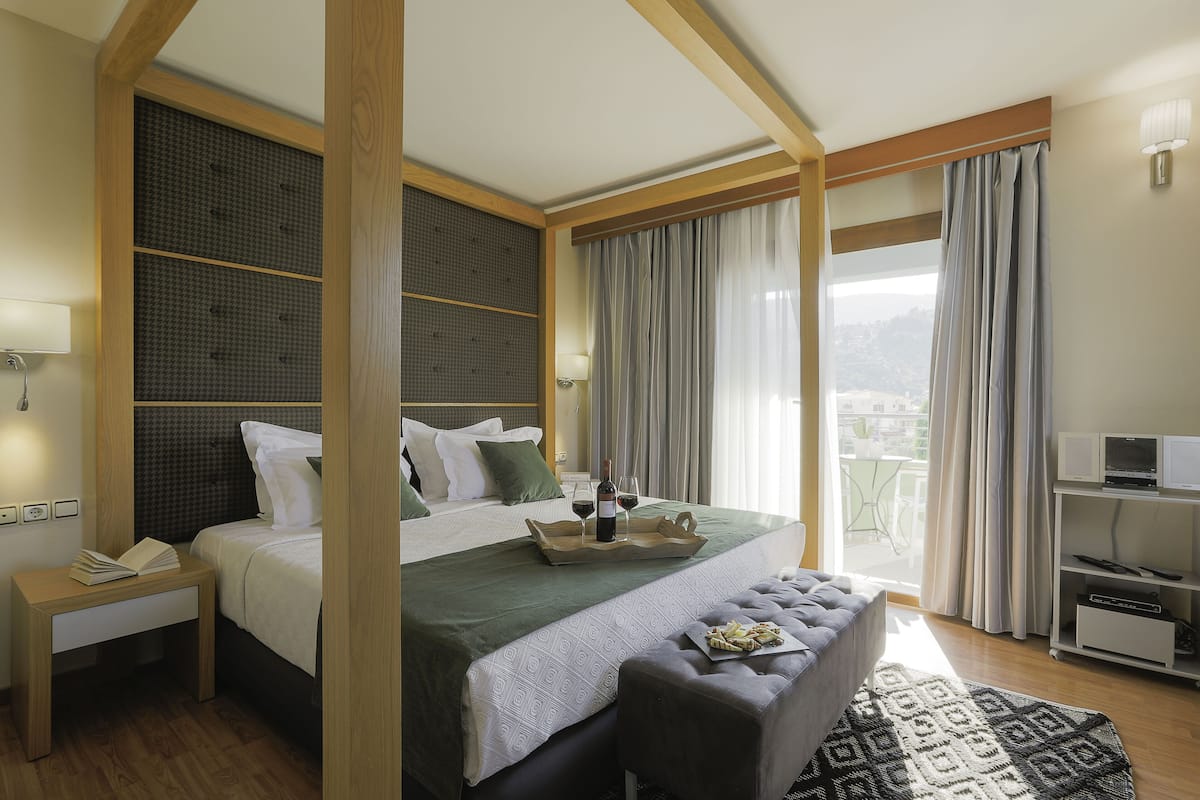 A modern hotel room with a large bed, a bedside table, a desk, a bench, and a TV.
