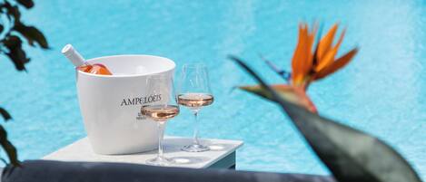 Un espacio junto a la piscina con un balde blanco que dice "AMPELOIS" y dos copas de vino sobre una mesa.