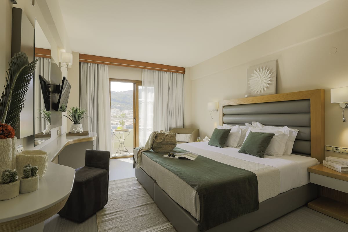 A modern hotel room with a large bed, a desk, a chair, and a view of the outdoors.