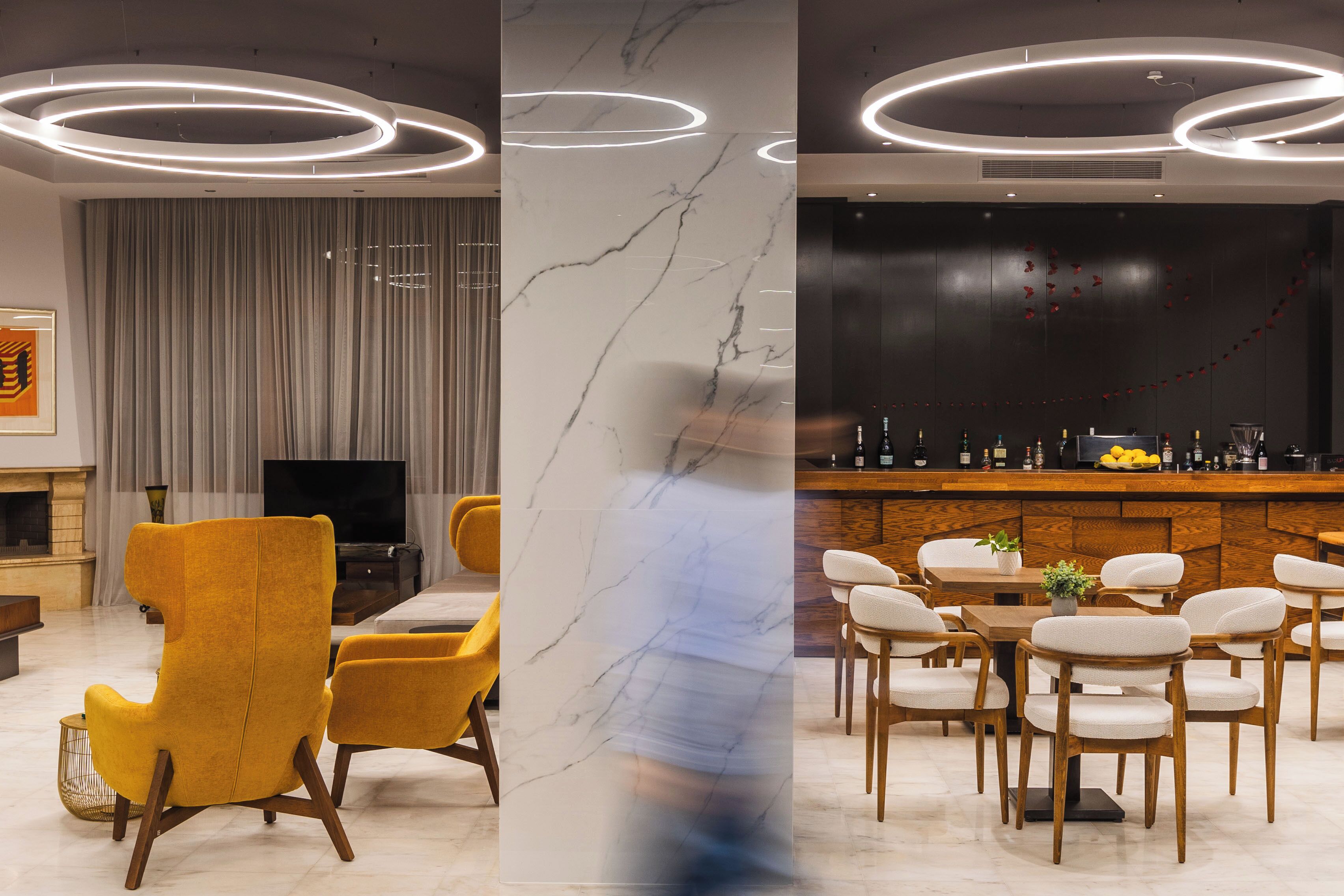 En moderne hotellobby med en marmorsøjle, et fjernsyn, et barområde og gule stole.
