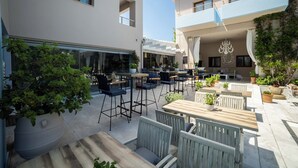 Un espace extérieur aménagé en patio, doté de plusieurs coins salon, notamment des tables et des chaises, et agrémenté de plantes en pot et d'une structure vitrée.