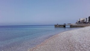 Una playa de guijarros con un muelle de hormigón que se adentra en aguas tranquilas.