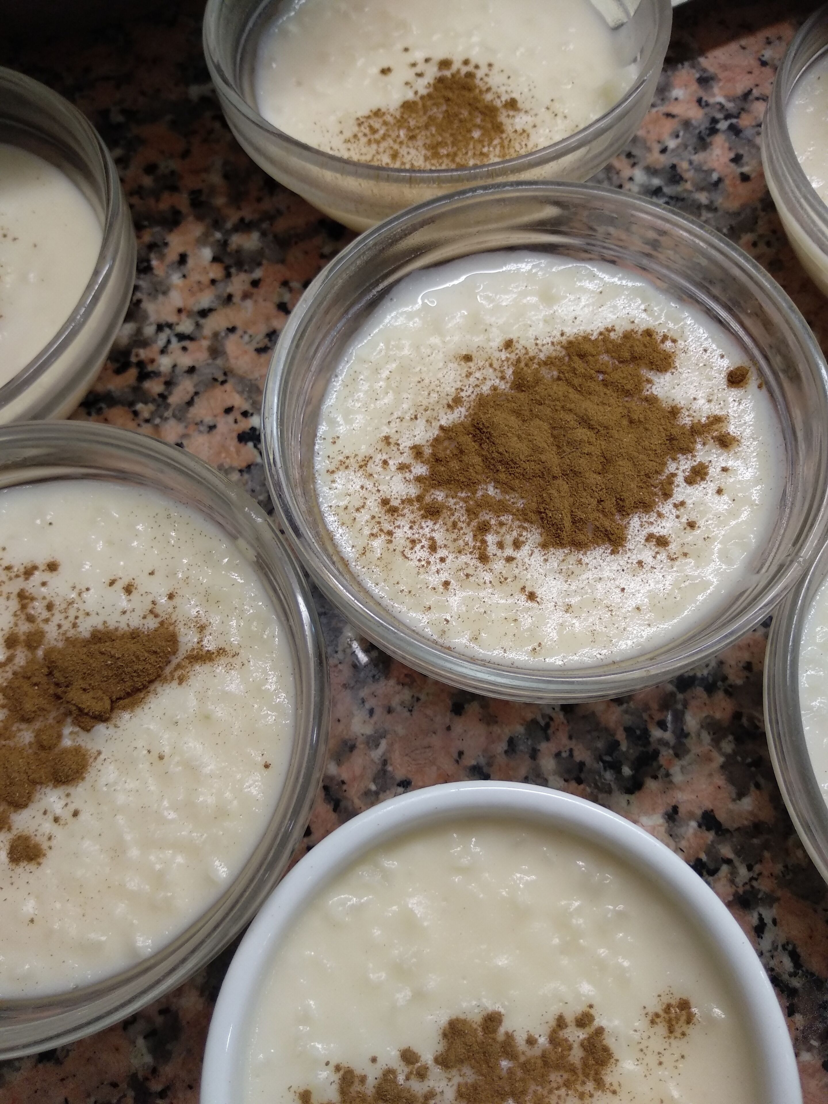 Several bowls of a creamy dessert topped with a brown powder, likely cinnamon, on a speckled countertop.
