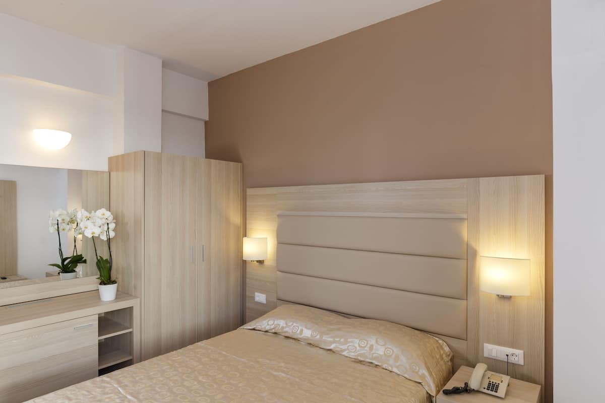 Ein Hotelzimmer mit Bett, Nachttisch, Lampe, Telefon und Spiegel.