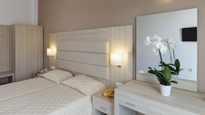 Una habitación de hotel con cama, mesitas de noche, un espejo y una orquídea en maceta.