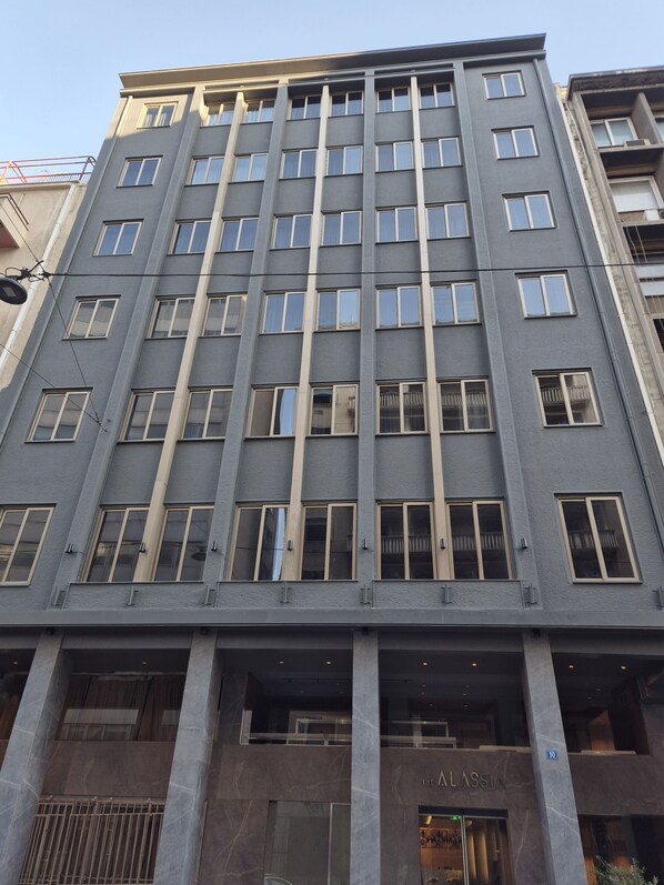 A multi-story building with a modern architectural design, featuring a series of evenly spaced windows and a prominent entrance with a nameplate. - THE ALASSIA HOTEL (Athens)