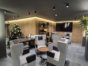 A modern lounge area with a Christmas tree, comfortable seating, a wooden table, a bookshelf, and a flat-screen TV. - THE ALASSIA HOTEL (Athens)