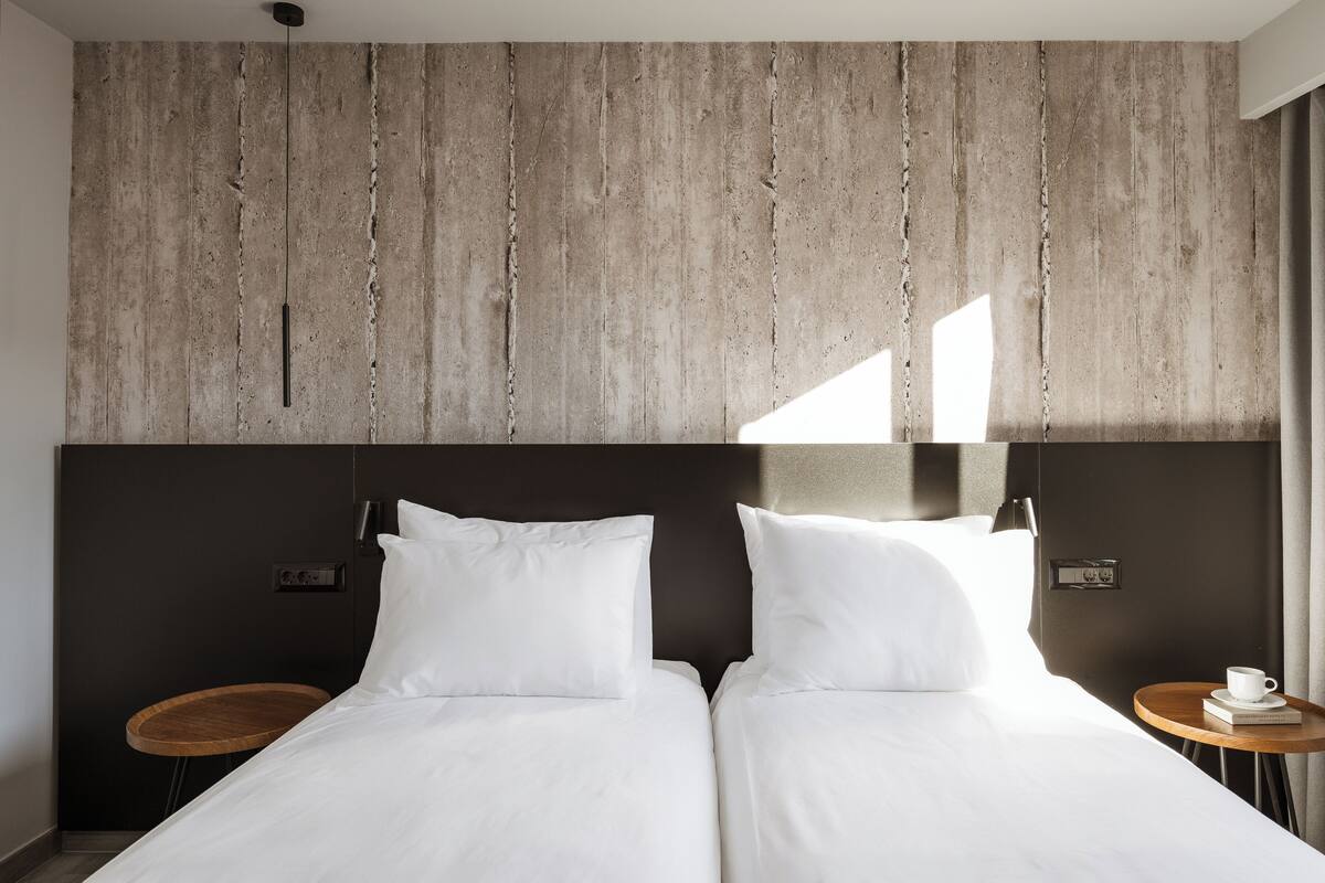 Una habitación de hotel moderna con una cama grande, dos mesitas de noche y un cabecero de madera.