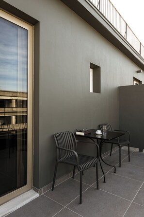 A modern outdoor seating area with two chairs and a table, a glass door, and a view of a building across the street.