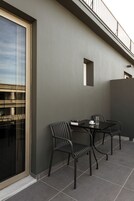 Uma área externa moderna com assentos, incluindo duas cadeiras e uma mesa, uma porta de vidro e vista para um edifício na rua.