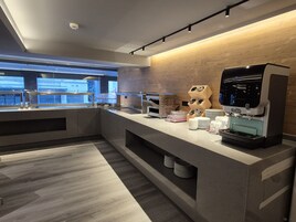 A modern kitchen area with a coffee machine, tea station, and a view of the cityscape through a window.