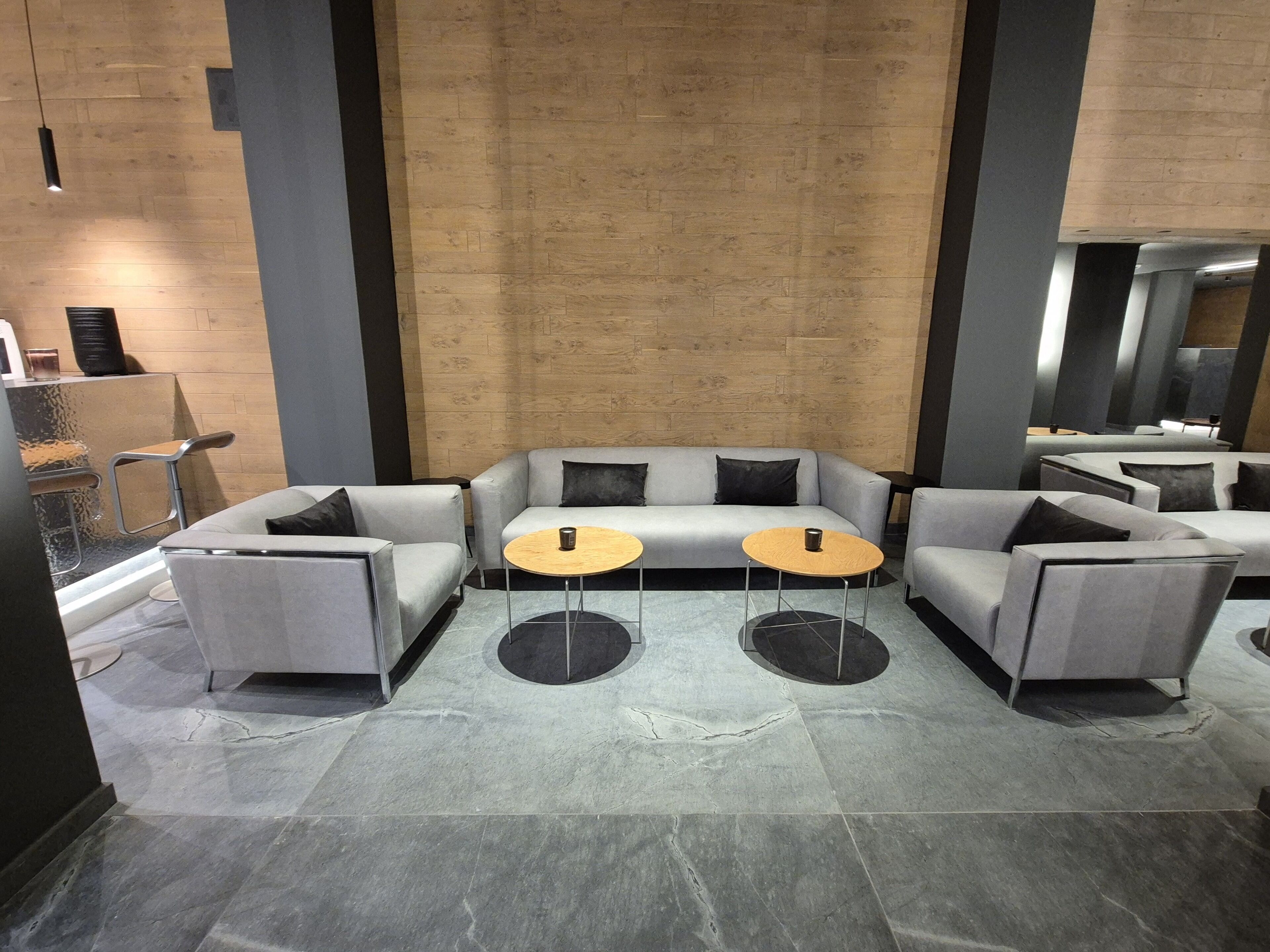 A modern lobby with grey sofas, two wooden tables, and a stone-tiled floor.