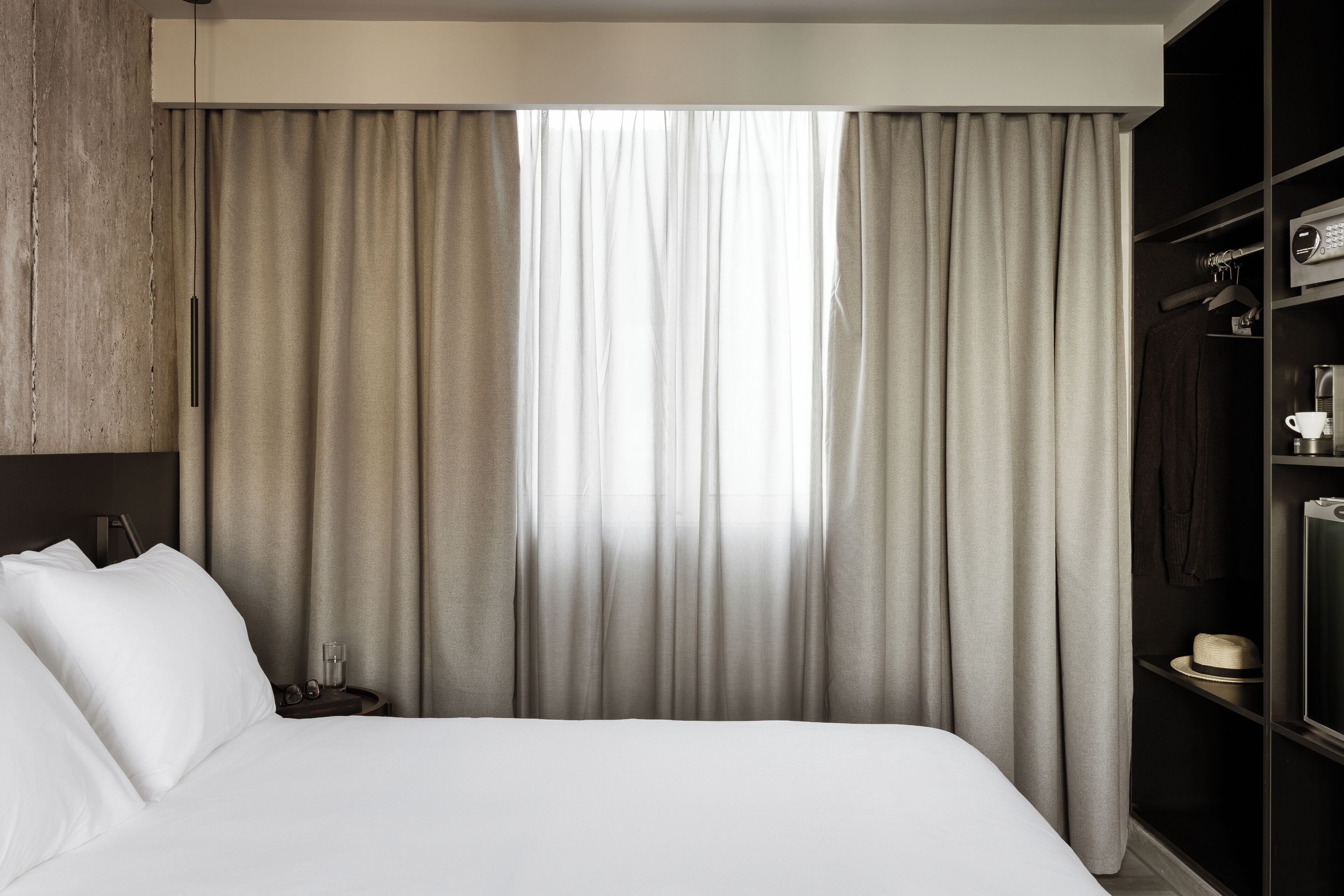 A hotel room with a large bed, a wardrobe, and a nightstand with a lamp.
