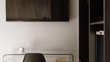 A modern room with a glass desk, a dark chair, a mounted TV, and a black shelving unit.