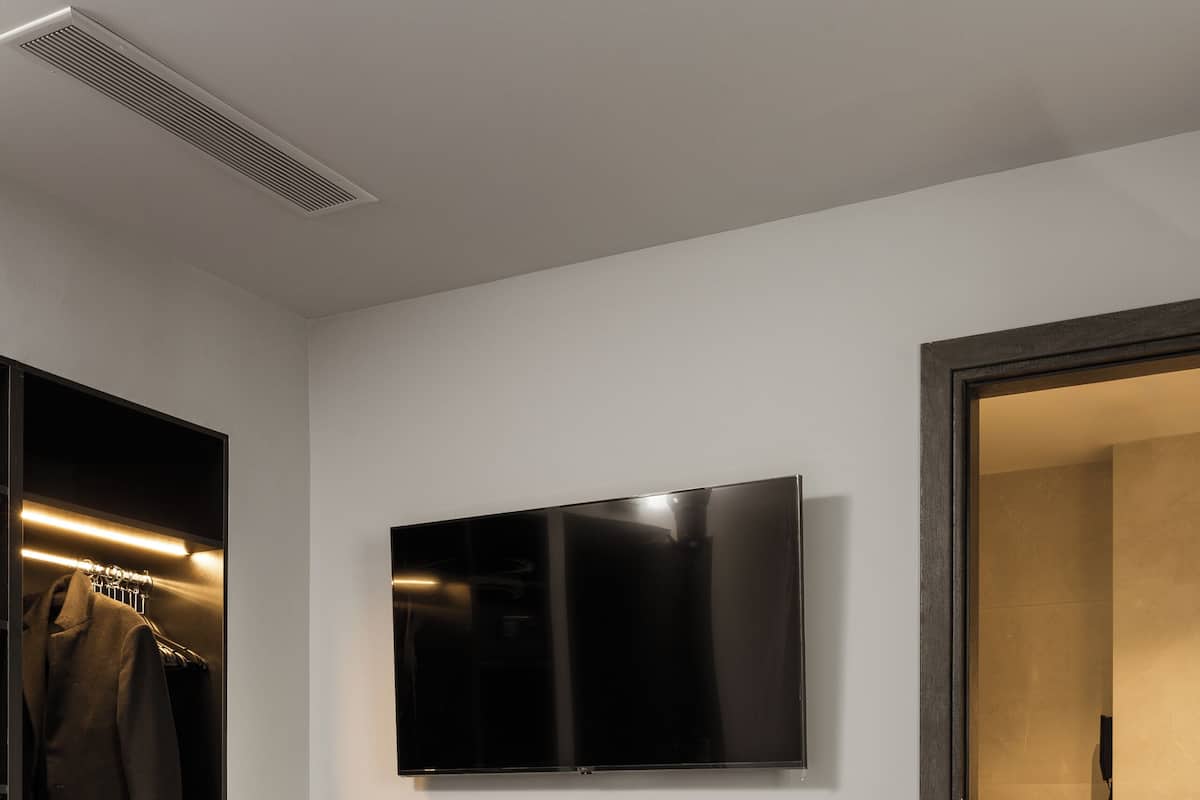 Una habitación de hotel moderna con escritorio de vidrio, televisor de pantalla plana, armario y baño a la vista.