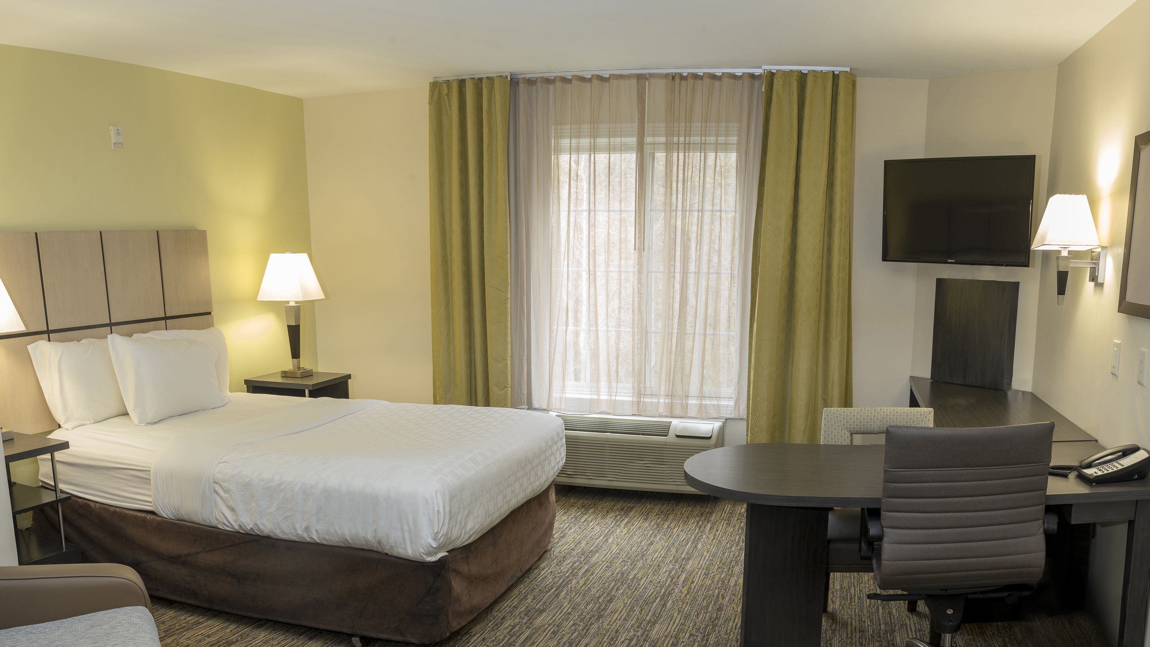 Habitación de hotel con cama, lámparas de noche, escritorio con silla, televisor y ventana con cortinas.