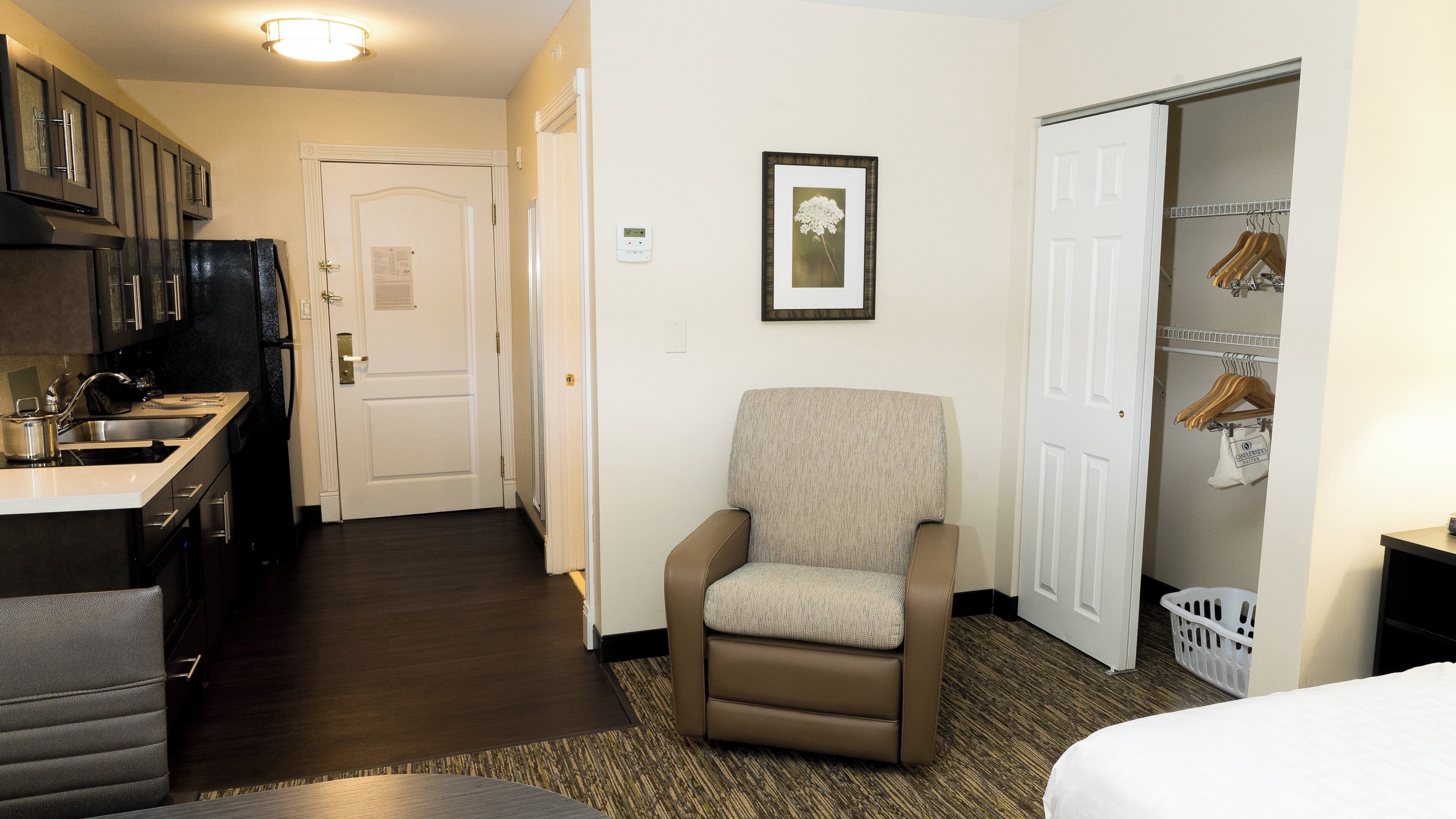 A hotel room with a kitchenette, a seating area, a wardrobe, and a framed picture on the wall.