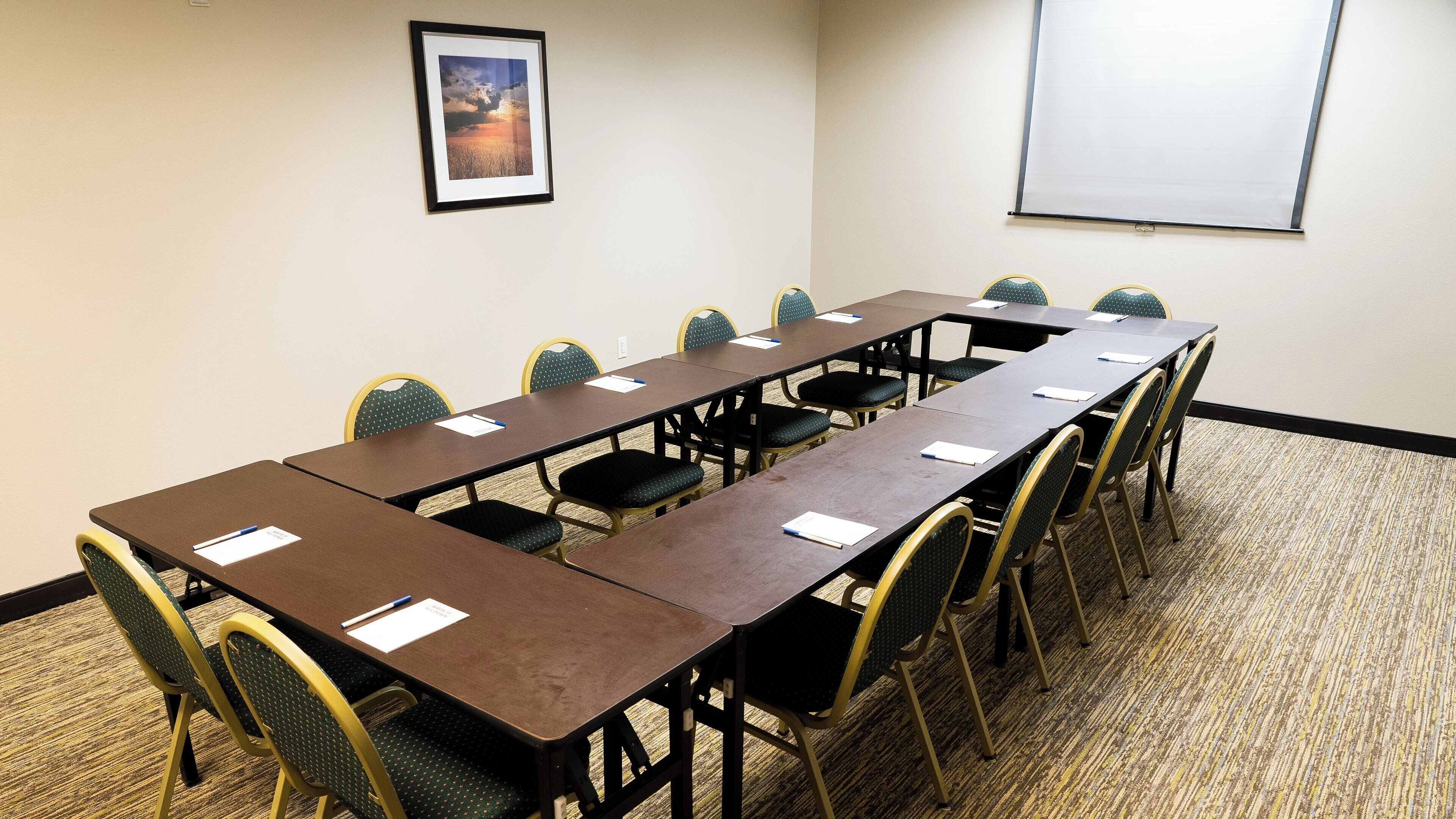 A conference room with a long table, chairs, a projector screen, and a framed picture on the wall.