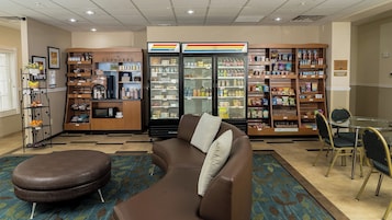 A hotel lobby with a kitchenette, a refrigerator, and a seating area with a couch and chairs.