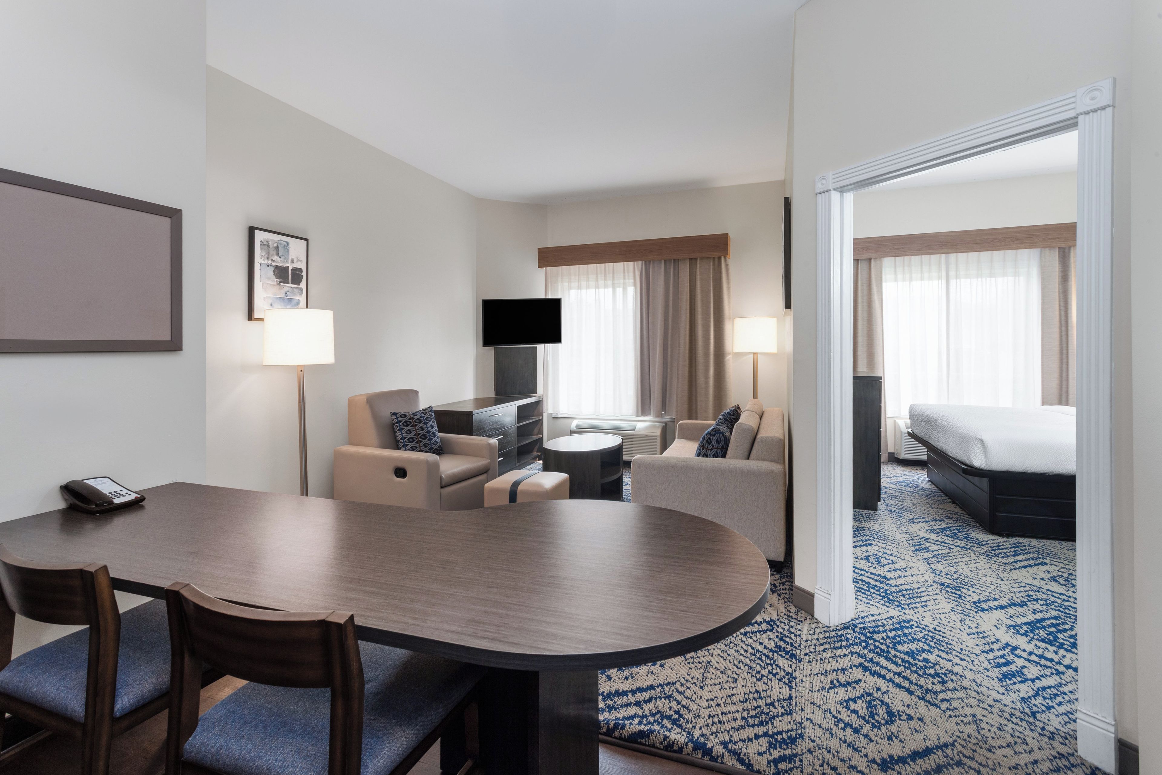 Habitación de hotel con zona de comedor, televisión, cama y baño.