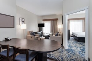 A hotel room with a dining area, a TV, a bed, and a bathroom.