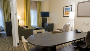 A hotel room with a round table, two armchairs, a sofa, a TV, a phone, and a painting on the wall.