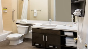 Un baño con inodoro, lavamanos y espejo. Se observan toallas y artículos de aseo.