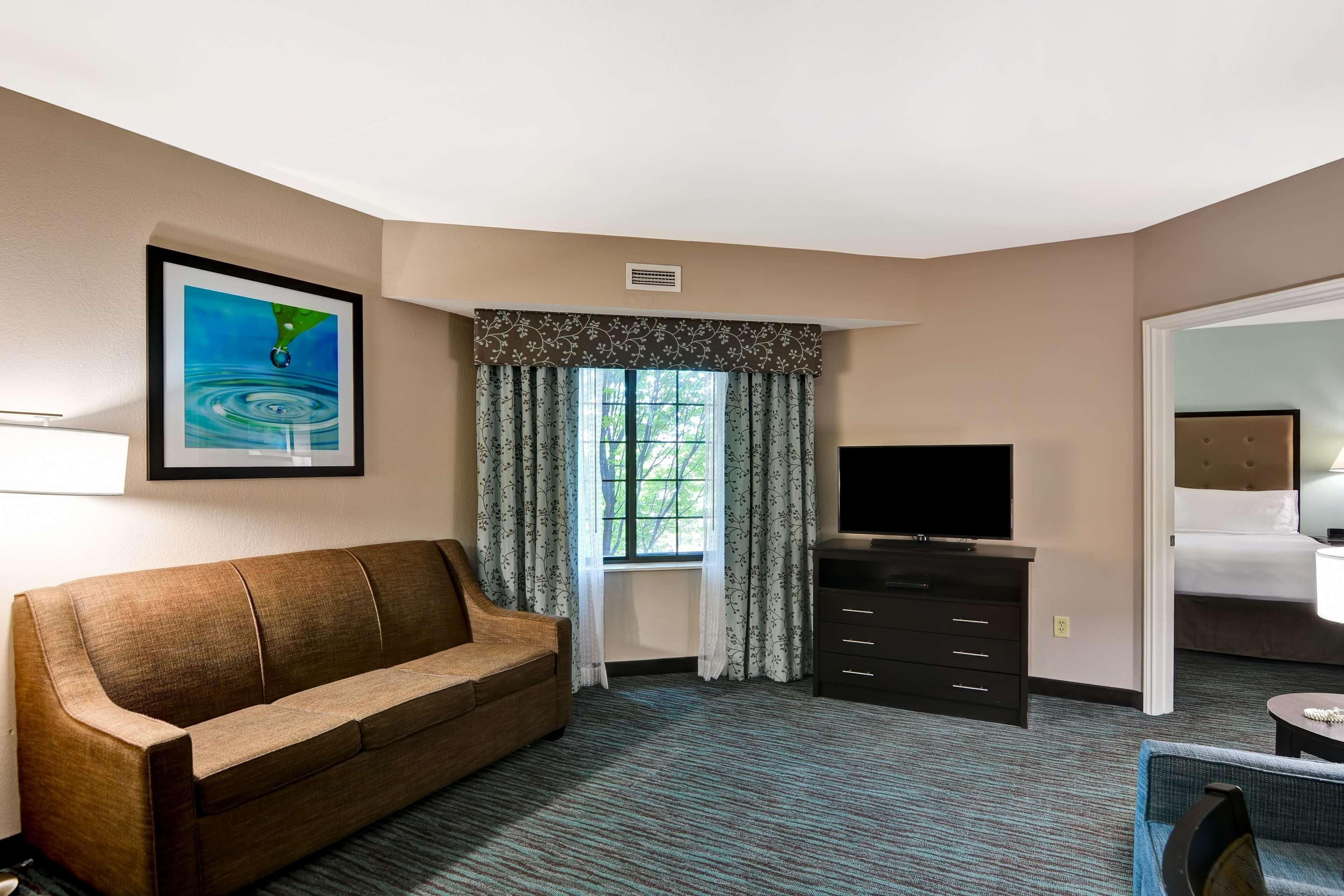 A hotel room with a sofa, a TV, a dresser, and a window with curtains.