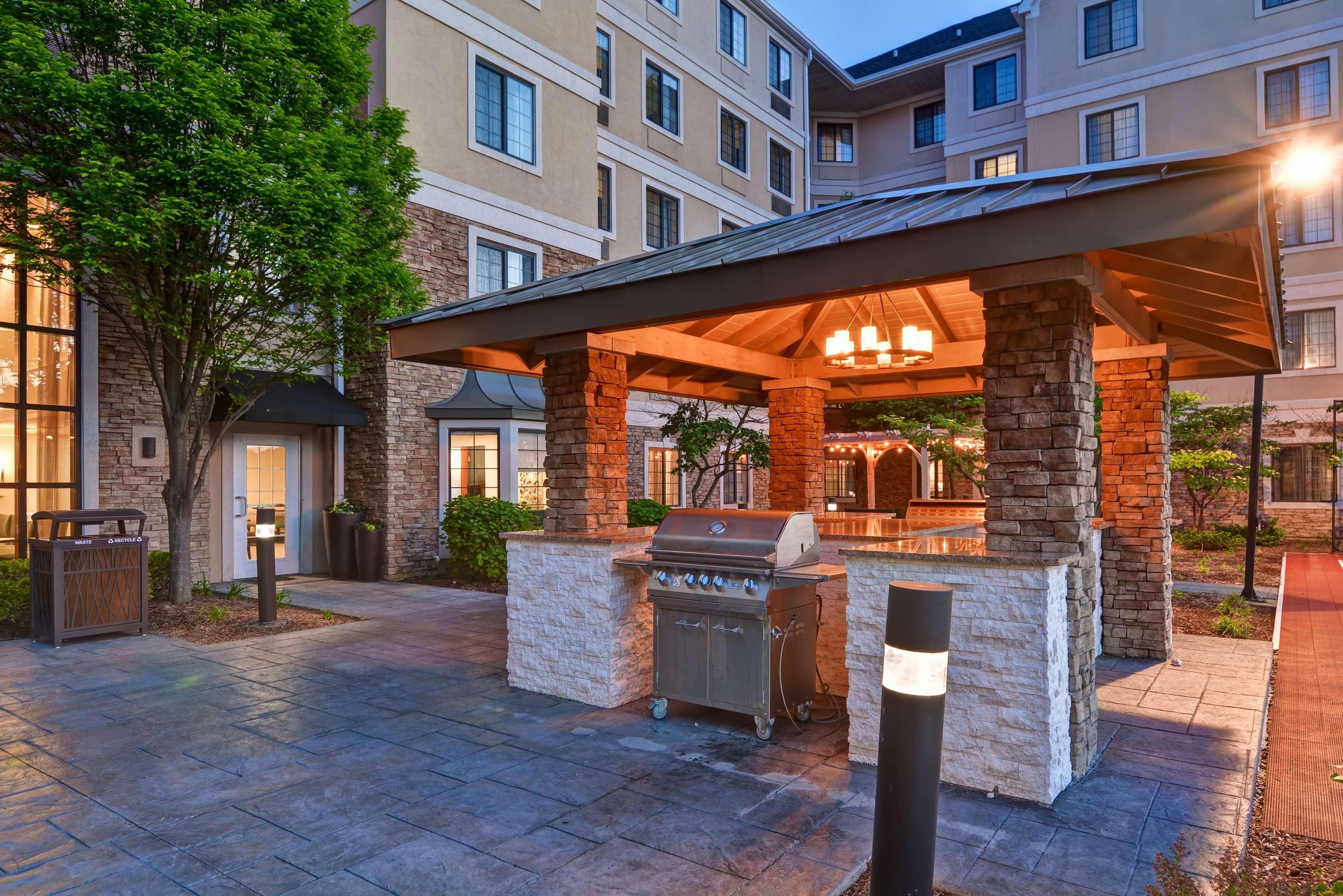 An outdoor patio area with a grill and seating, surrounded by stone pillars and a covered structure.